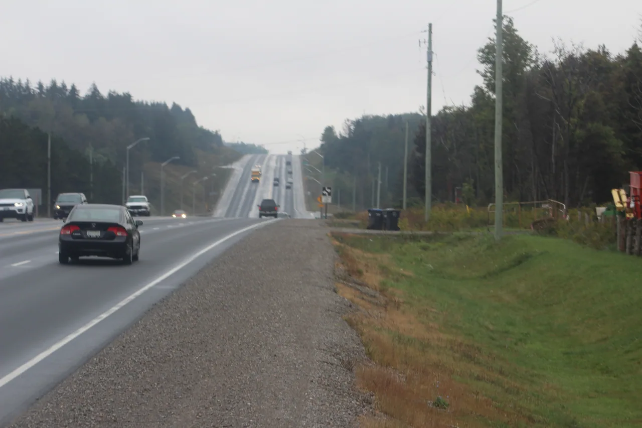 Cars travelling on a rolling rural highway bordered by trees in Caledon, Ontario.